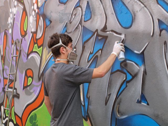 Ragazzo che munito di bomboletta spray sta ultimando un grande graffito su un muro della città
